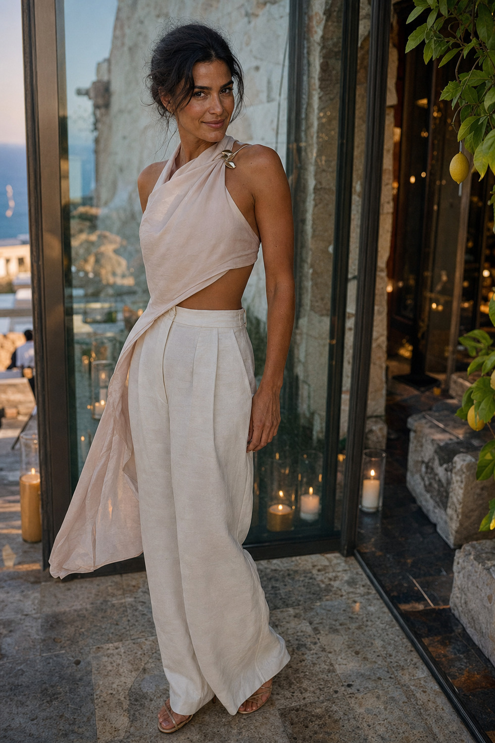 A woman in a blush scarf top and ivory trousers outside a glasshouse club.