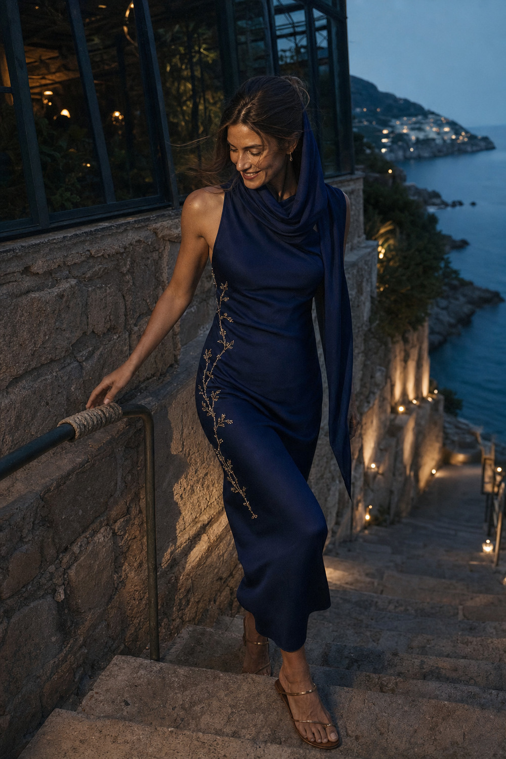 A woman in a cobalt scarf dress descending a stone stair toward the cove.